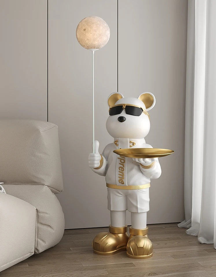 An anthropomorphic bear figurine dressed in white and gold, holding a golden plate and a staff topped with a moon, stands in a modern room, emitting a soothing glow.