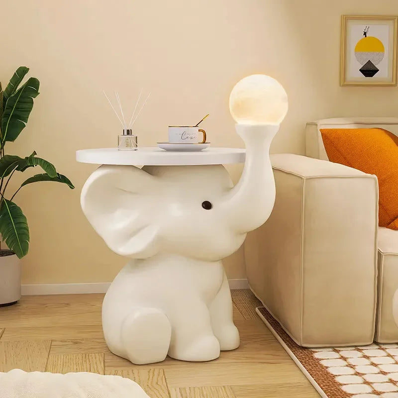 An elephant-shaped lamp with a glowing orb on its upturned trunk, standing next to a sofa in a bedroom decorated with warm tones.