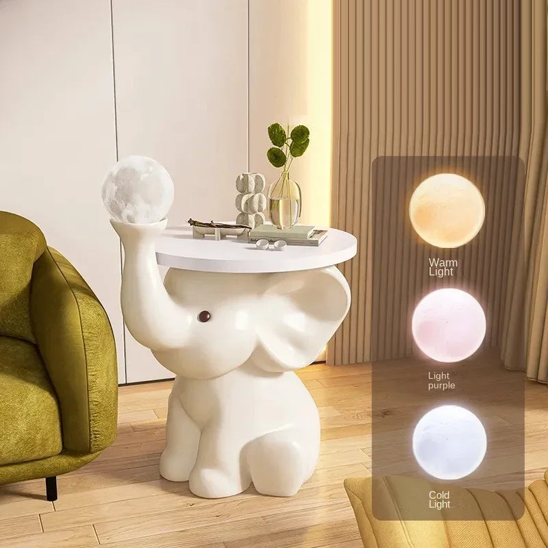A charming design white Elephant Bedside Table holding a moon lamp, with color lighting options displayed; placed in a cozy bedroom corner.