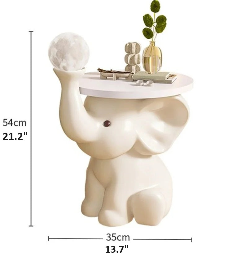 A decorative Elephant Bedside Table holding a lamp, books, and a small plant, with dimensions labeled in centimeters and inches.