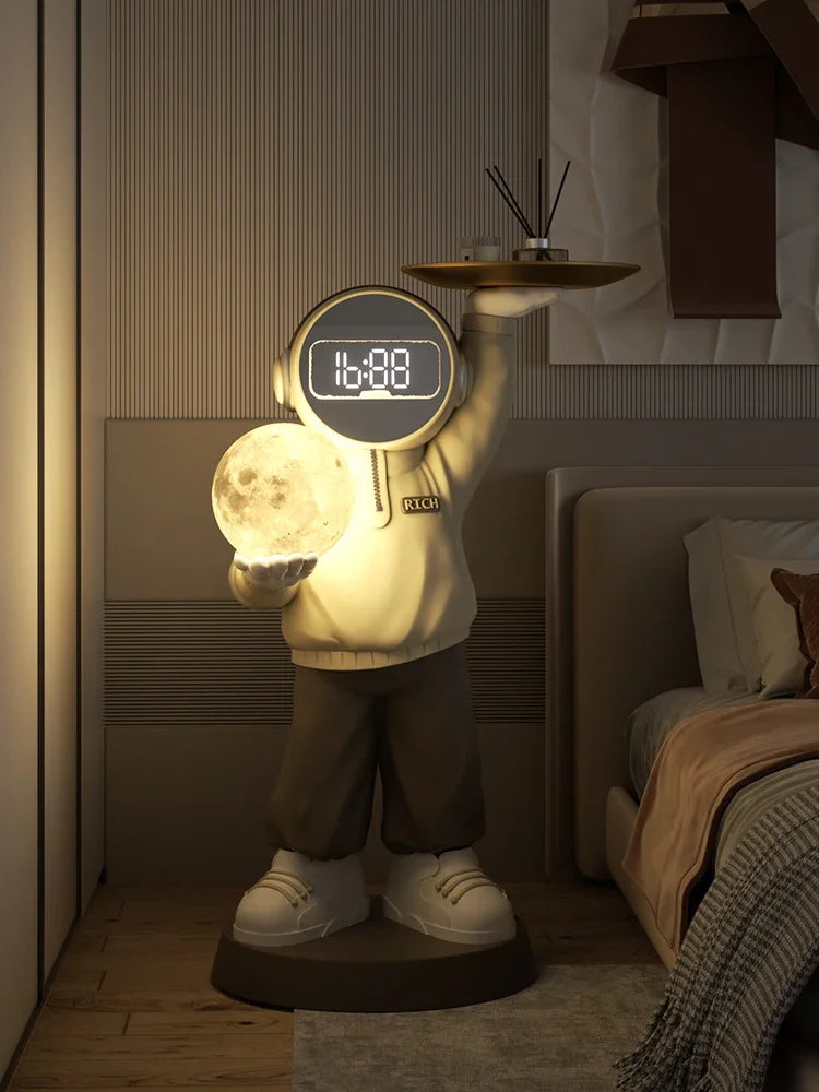 A soothing night light shaped like a cartoonish figure holding a glowing moon, with a digital clock display on its head, positioned next to a bed in a dimly lit room.