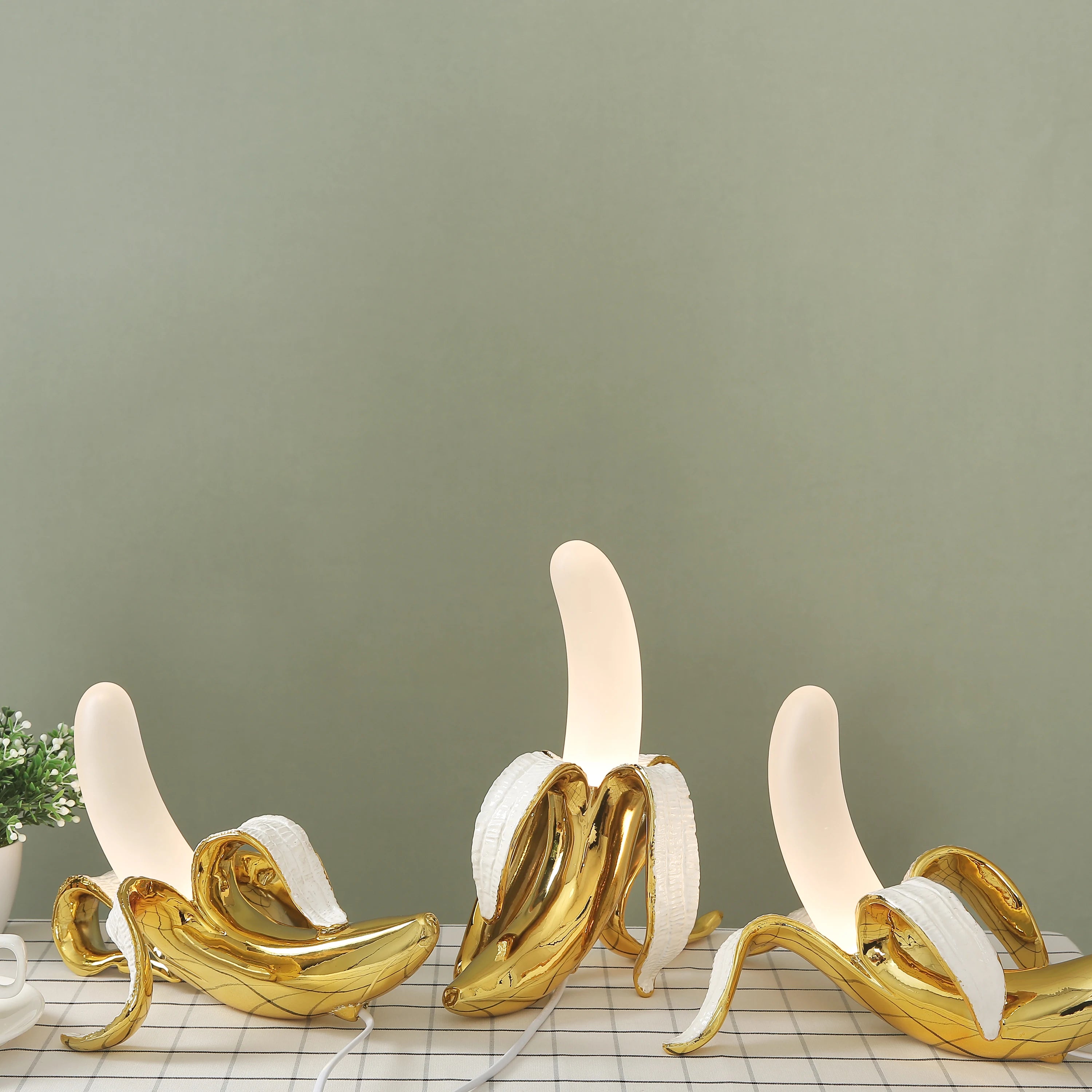 Golden banana peel table lamps emitting soft light on a table against a green wall, creating a cozy atmosphere.