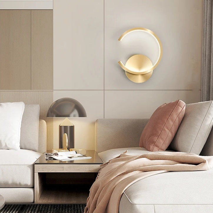 A contemporary living room with a white couch and a gold wall lamp that illuminates the space.