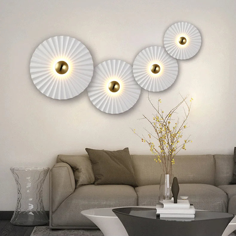 A modern living room with a beige sofa, decorative pillows, a clear side table, and four Origami Circle Wall Lights above the sofa. In the foreground, a vase with branches is placed on a coffee table.