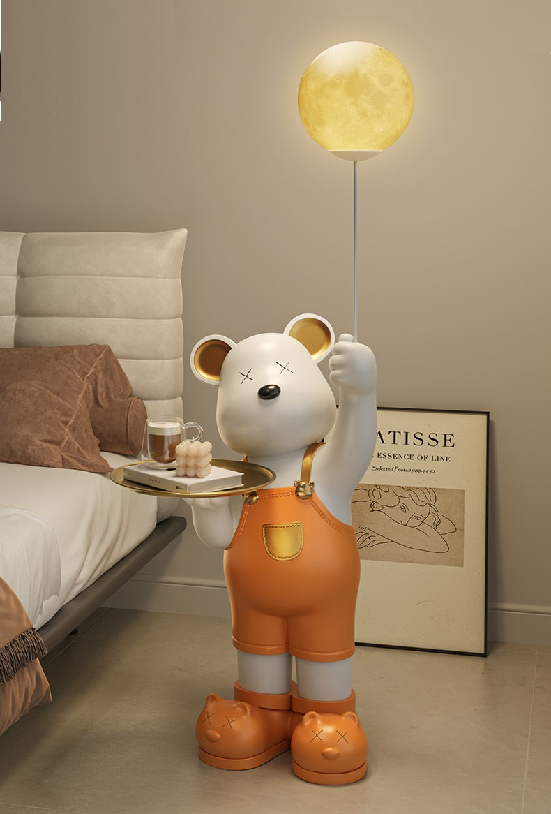 Decorative standing bear statue lamp with a moon-like light on a pole, holding a tray beside a bed in a dimly lit room.