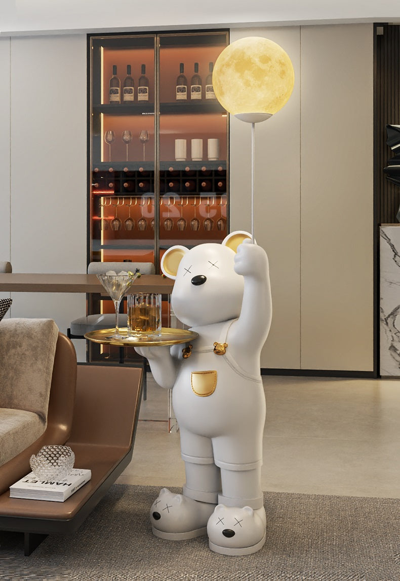 A whimsical Standing Bear Statue of a white bear holding a tray of drinks, with a moon-shaped balloon attached, placed in a luxury modern living room with a bar in the background.