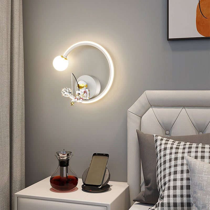 A modern Star Astronaut Wall Light above a bedside table with decorative items and a mobile phone charging, inspiring celestial wonder for aspiring astronauts.