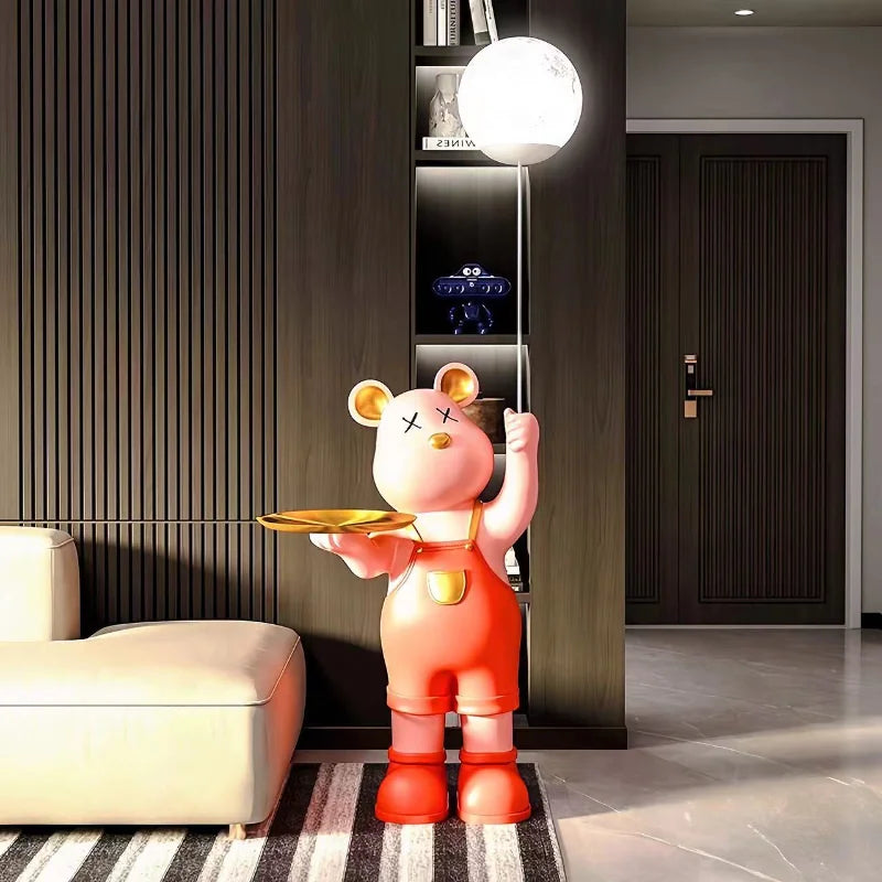 A luxury decorative floor lamp designed like a standing bear statue in red overalls, holding a serving tray, in a modern living room.
