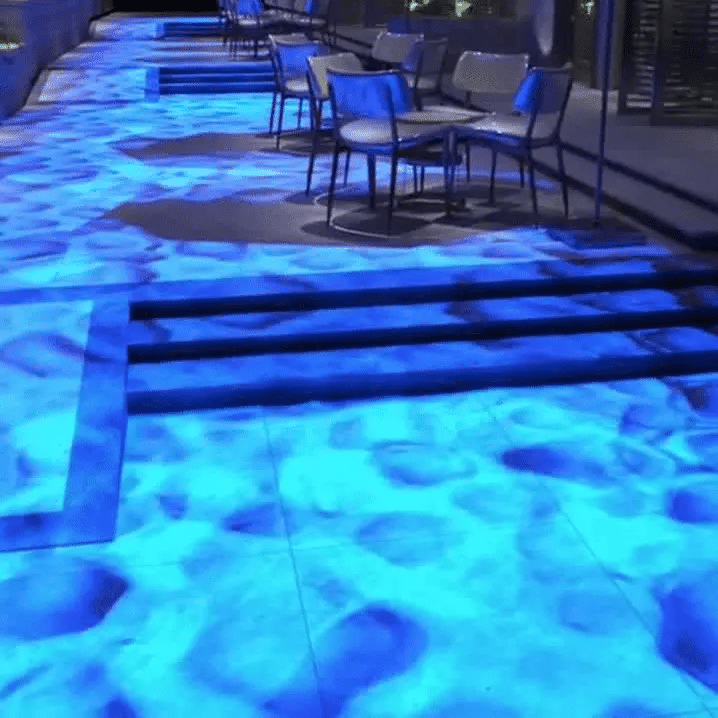A pathway illuminated with ambient light simulating water, featuring stairs and chairs along the sides.