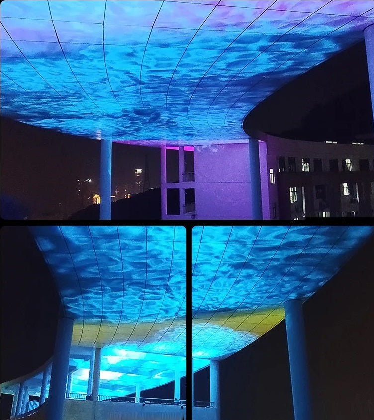 An outdoor installation featuring a large ceiling projection of a dynamic blue pattern using a Water Ripple Projector, viewed at night under a modern building with columns.