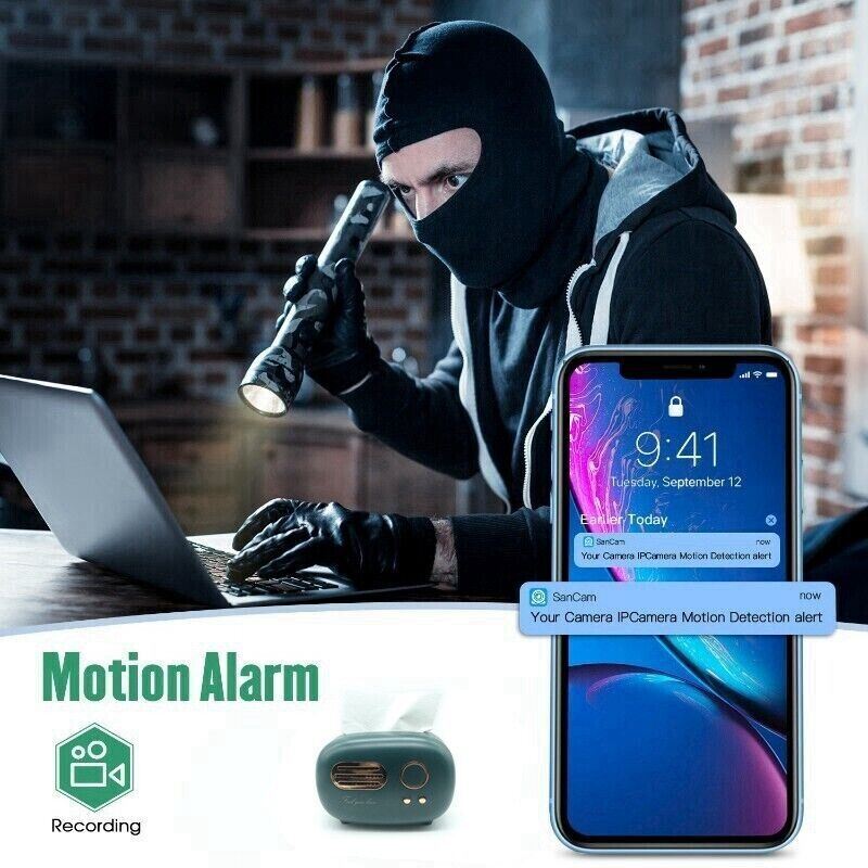 A masked intruder using a laptop next to a smartphone displaying a security alert notification from a Tissue Box SpyCam.