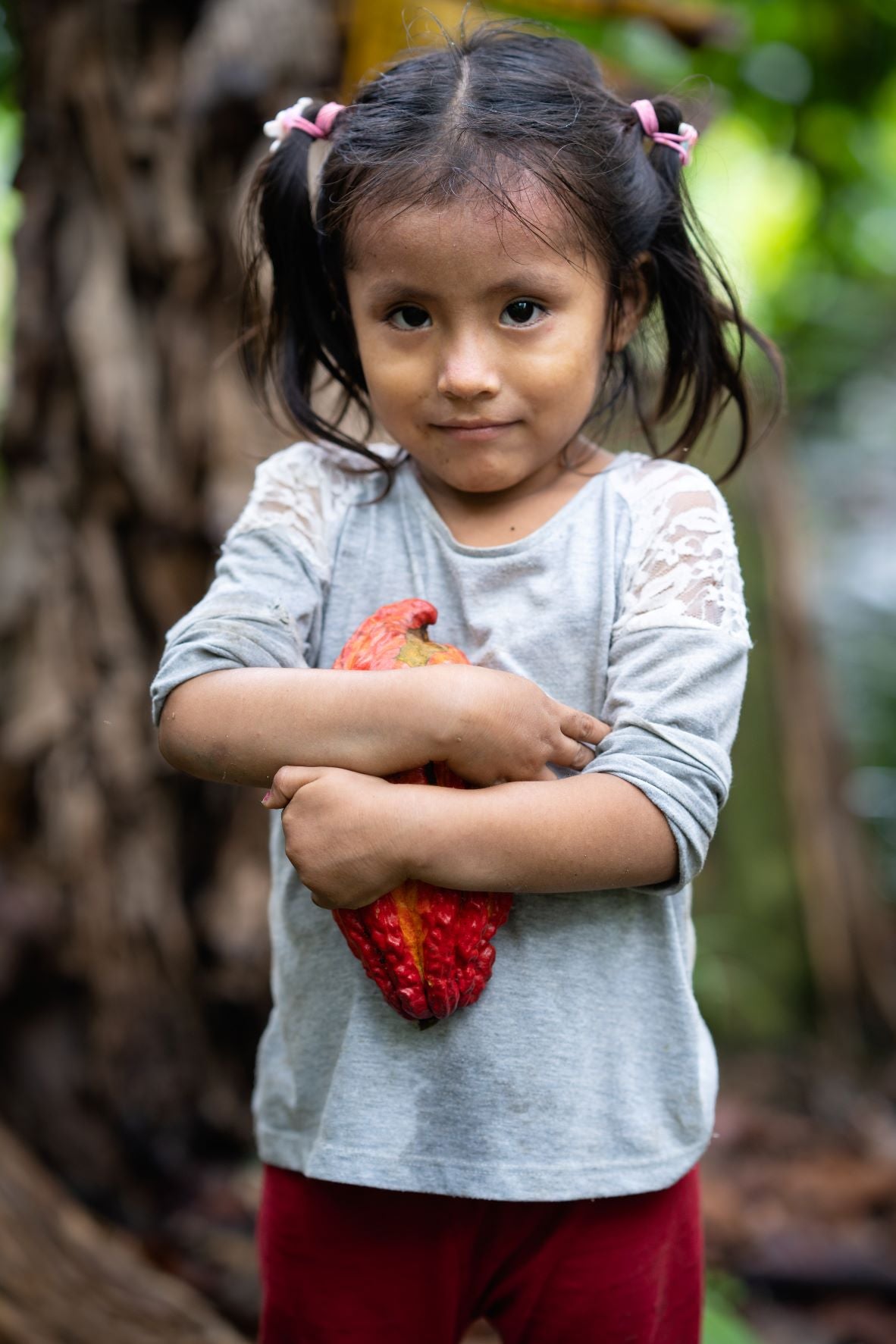 A cute dark-haired girl in the forest, hugging the fruit in her hand, looks at the camera with a smile.