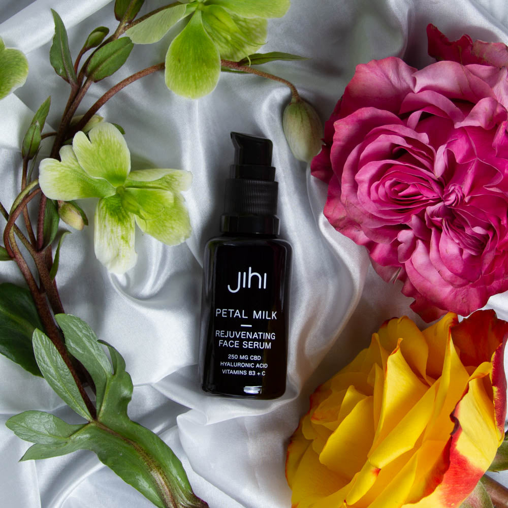 Jihi Petal Milk Rejuvenating Face Serum on silk surrounded by flowers