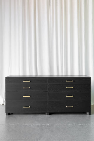 Black wooden sideboard, with visible wood grain. 8 drawers, antique brass handles and geometrical feet