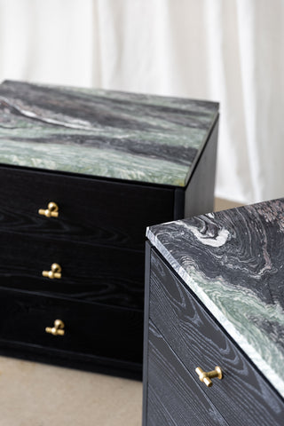 Pair of black wooden bedside cabinets with 3 drawers each, brass T-shaped handles and marble tops