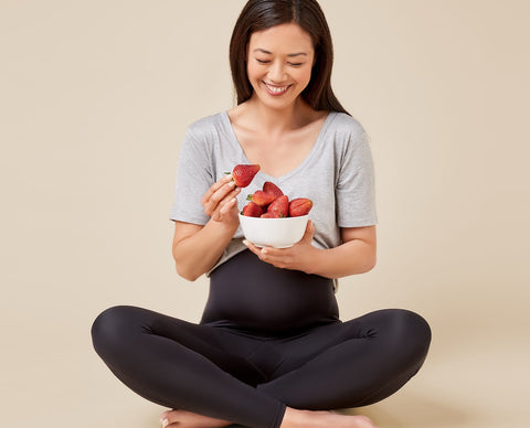 Pregnant mama eating strawberries in TheRY maternity leggings