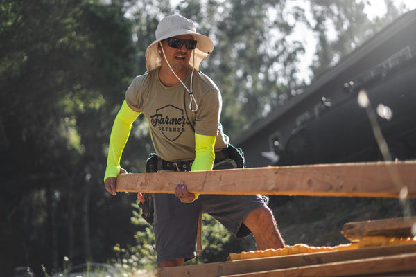 A man hauling lumber on a construction site wearing protective sleeves.