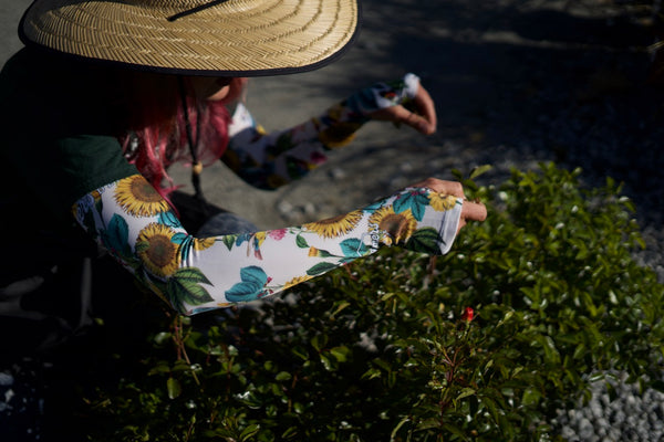 Someone wearing gardening sleeves trimming a bush. 