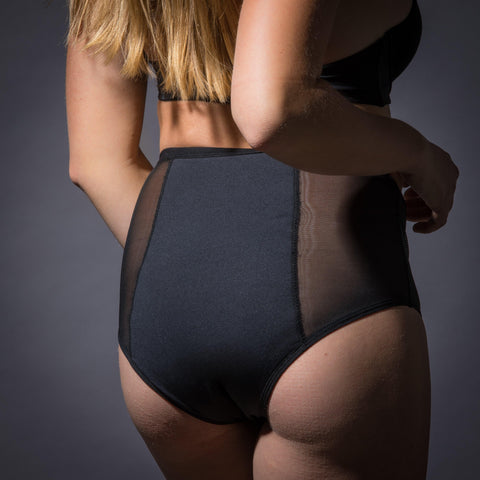 Model wears Heralogie's Stacie High Rise Brief in black. The underwear is constructed with 2 mesh panels flanking a central, absorbent panel. The materials are body safe, nontoxic, and ecofriendly.