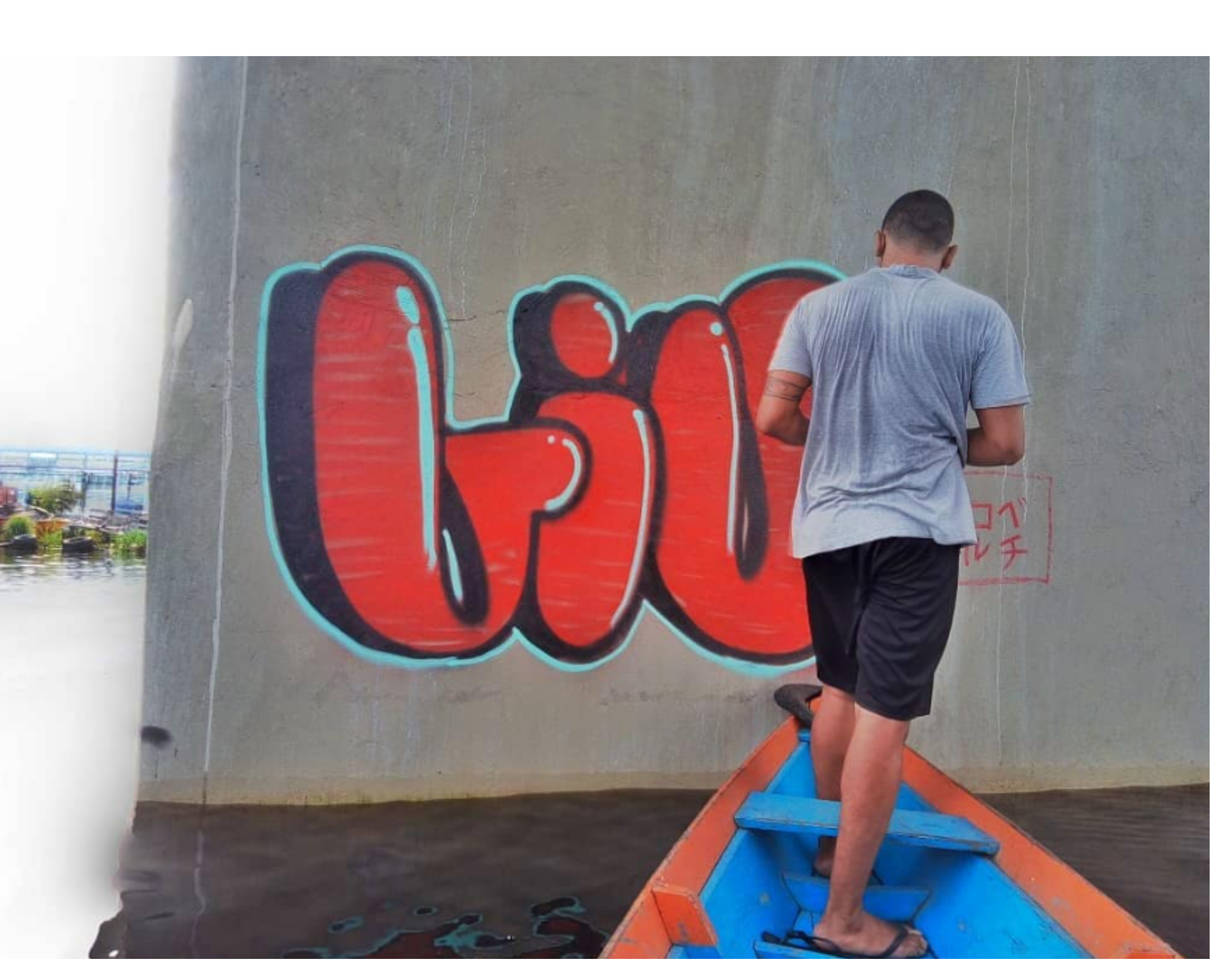 Foto do artista em pé numa canoa grafitando na coluna da ponte do rio negroliu bomb 3