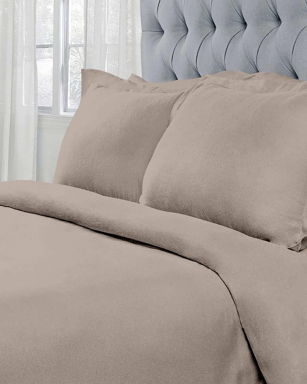 Taupe bedding from St. Pierre, featuring a cozy duvet and matching pillows, styled against a tufted grey headboard.