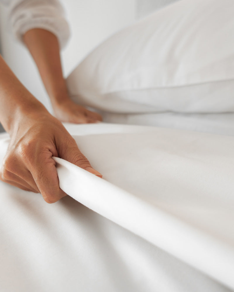 Female hand set fluffing up the white sheet on the bed