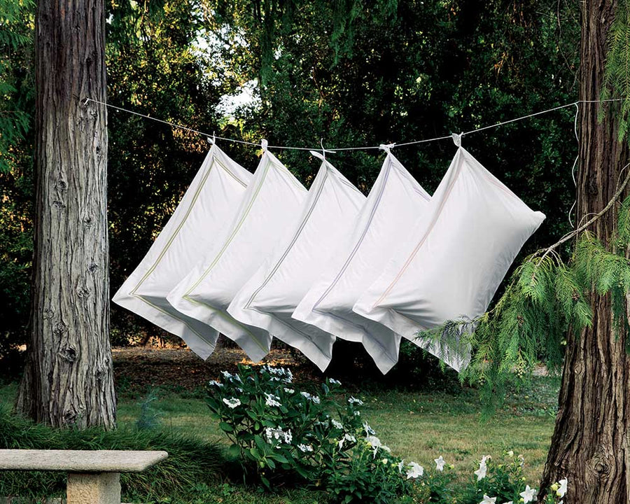 Five pillows with an edged double embroidered line-drying between two trees surrounded by nature