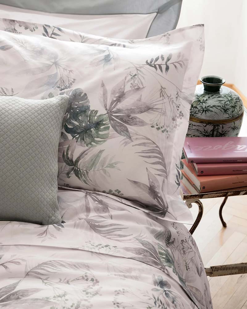 Blue and white Cotton Sateen bedding from Fazzini next to a table with books and a porcelain vase.