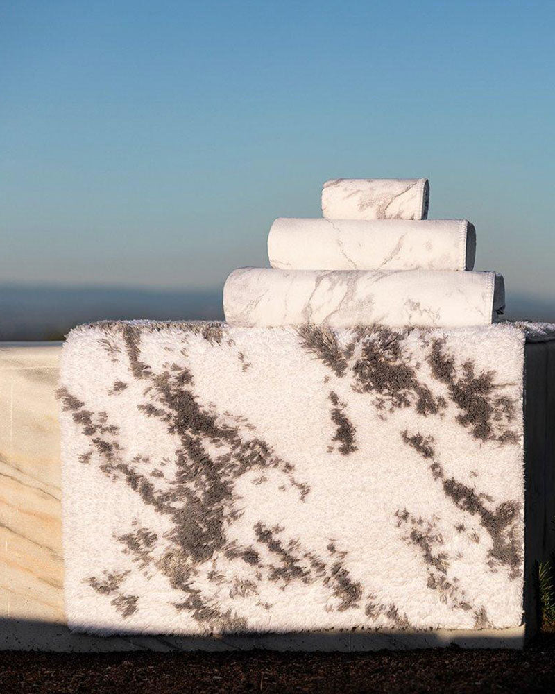 Marble-patterned bath rug and towels in the same hue on a wall overlooking the sky.