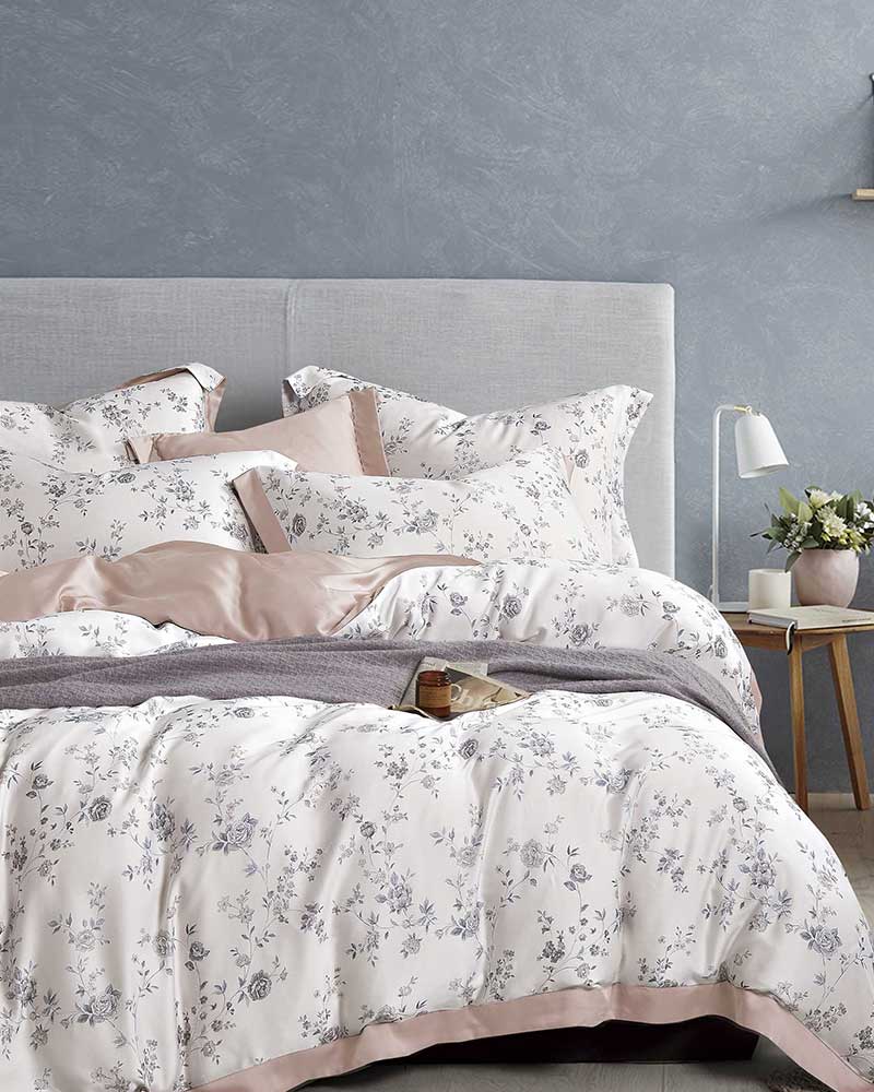 White and pink Micromodal bedding from St. Pierre in a bedroom with a grey wallpaper and wooden furniture.