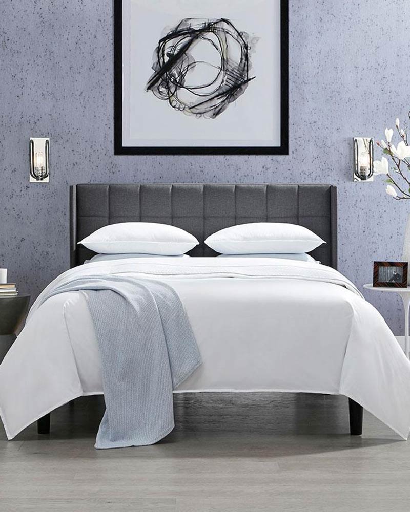 White bedding from Sferra in a bed with fabric headboard next to two bedside tables.