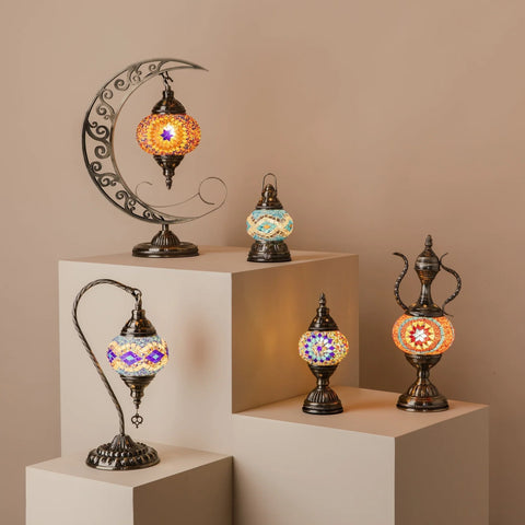 A collection of five ornate lamps displayed on white pedestals against a beige background.