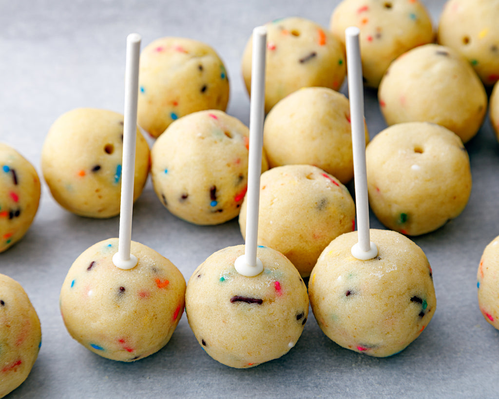 Securing each cake pop ball to a stick using melted chocolate