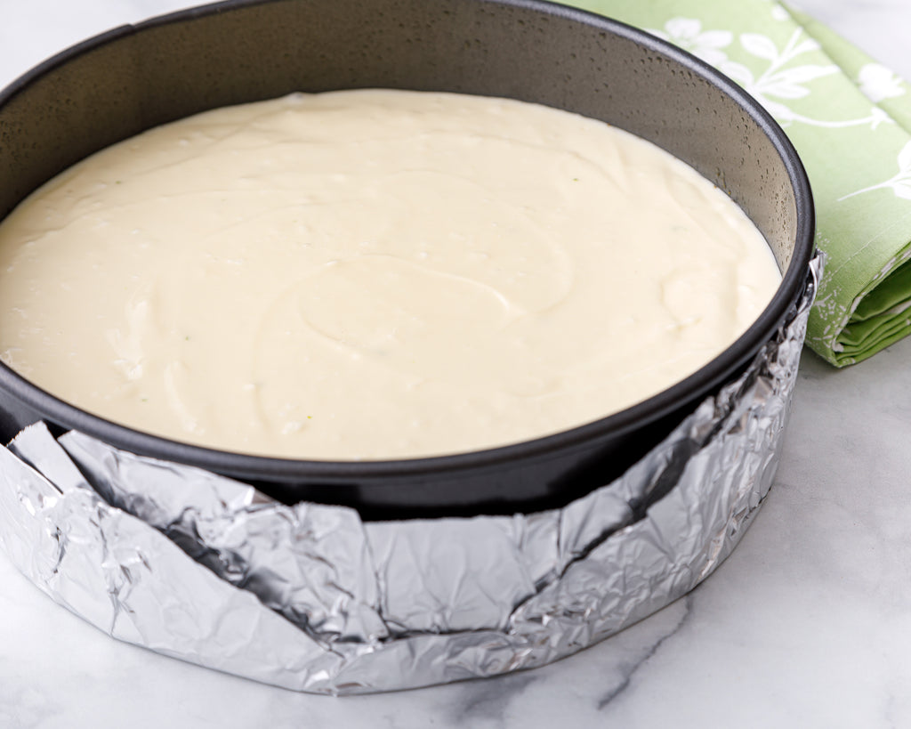 Finished cheesecake batter in springform pan wrapped in aluminum foil