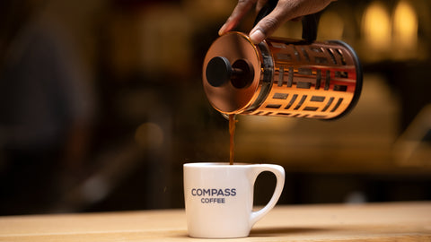 French press pouring coffee into a compass mug