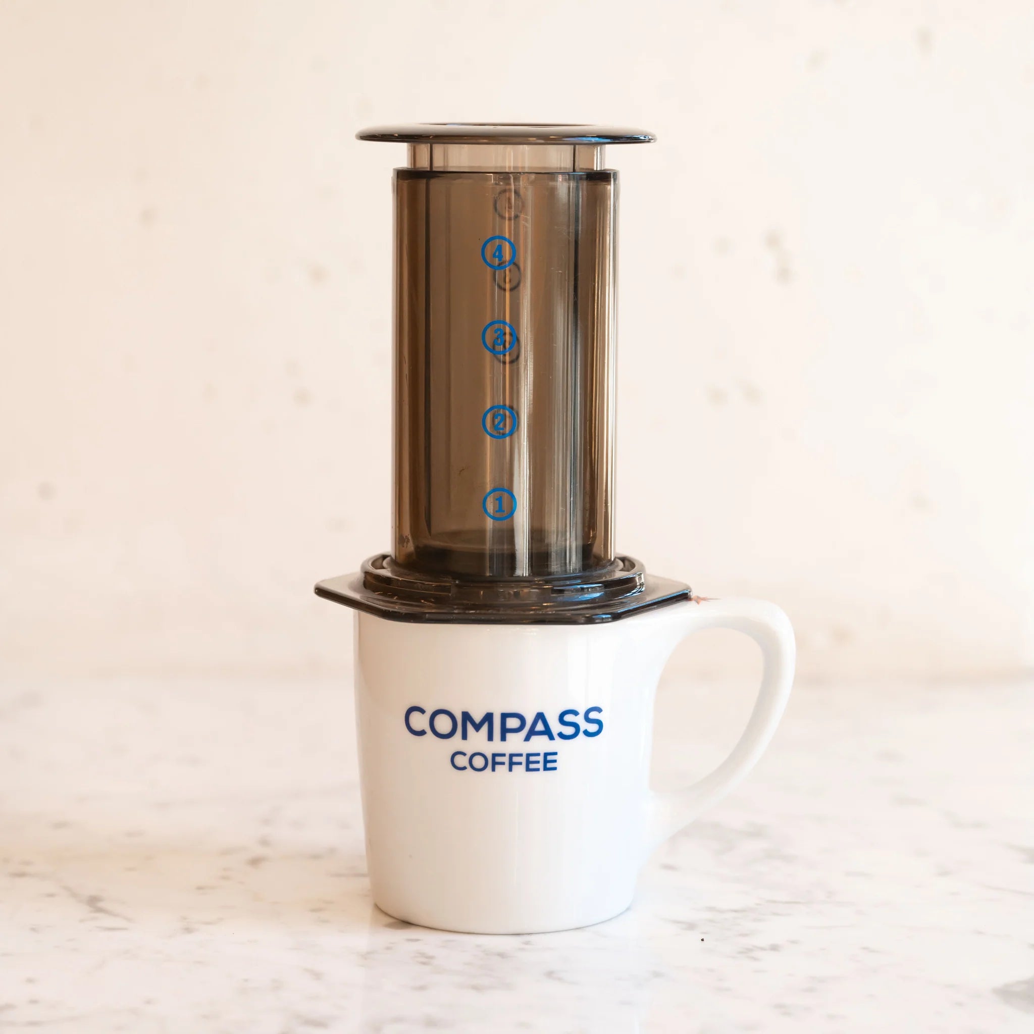 An aeropress pouring coffee into a Compass Coffee mug.