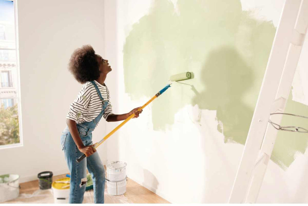 A person using a paint roller to paint a wall green