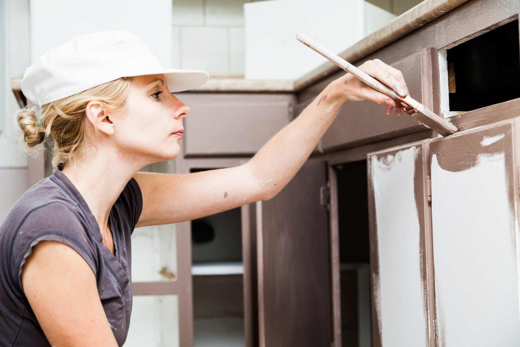 Woman painting kitchen cabinets with brown Benjamin Moore Advance Paint