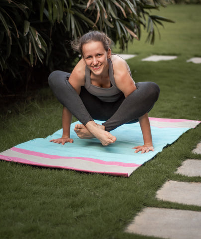 yoga teacher in organic tshirt, shows how to do bhujapidasana pose on the pvc free yoga mat during the yoga class outdoors