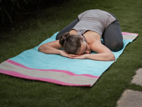 Girl resting during her yoga vinyasa practice on organic cottom mysore yoga rug in Balasana pose. Also known as Child pose