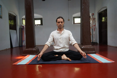 Ashtranga Yoga teacher sitting in siddha yoni asana on yoga rug on the red floor. Practicing Pranayama practice