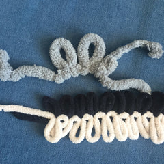 Two brands of loop yarn against a medium-blue background, the larger grey and single-stranded, the smaller double-stranded and black and beige.