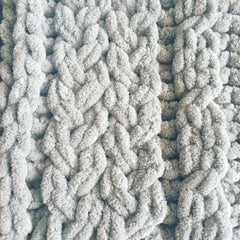 A close up of knitting detail showing grey chenille yarn in a braided pattern