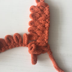 Orange chenille loop yarn showing a row of knit stitches. The row of stitches lie vertically with the working yarn lying perpendicular to the left.