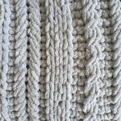 A close up of knitting detail of grey chenille yarn in a mix of cable styles.