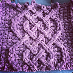 A close up of knitting detail showing mauve chenille yarn in a Celtic Cable Saxon Braid design.