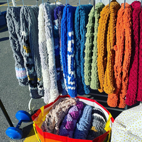 A rack of different colours of knitted chenille blankets, arranged in a rainbow