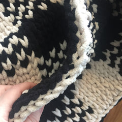 Edge of a black and beige knit blanket showing a double-bound edge.