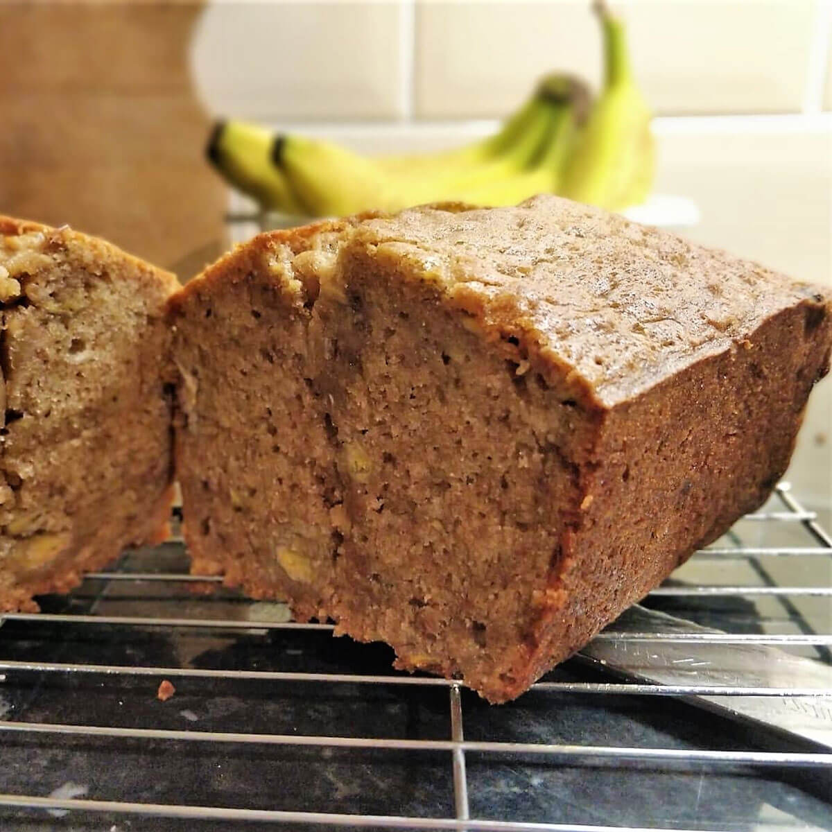 Final result of banana bread, sliced open with bananas in the background