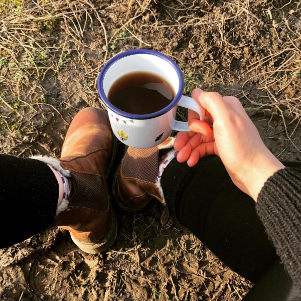 A person holding a cup of tea in a tin mug.